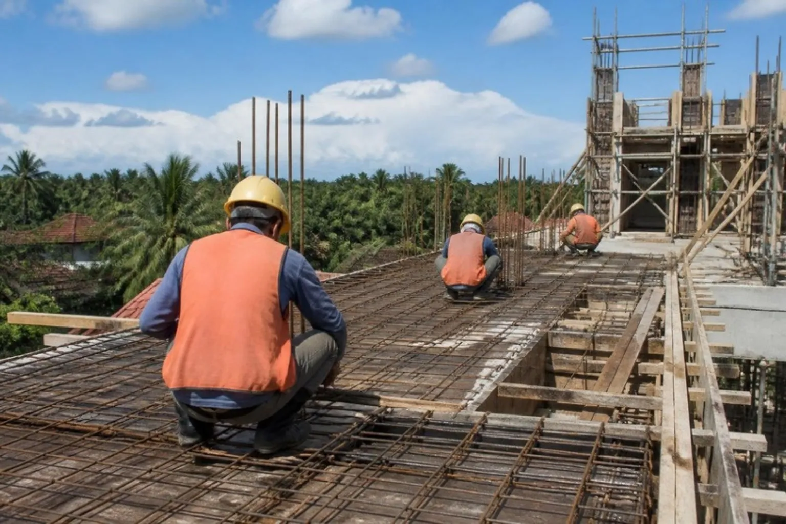 Workers in helmets tying steel reinforcement for a floor slab